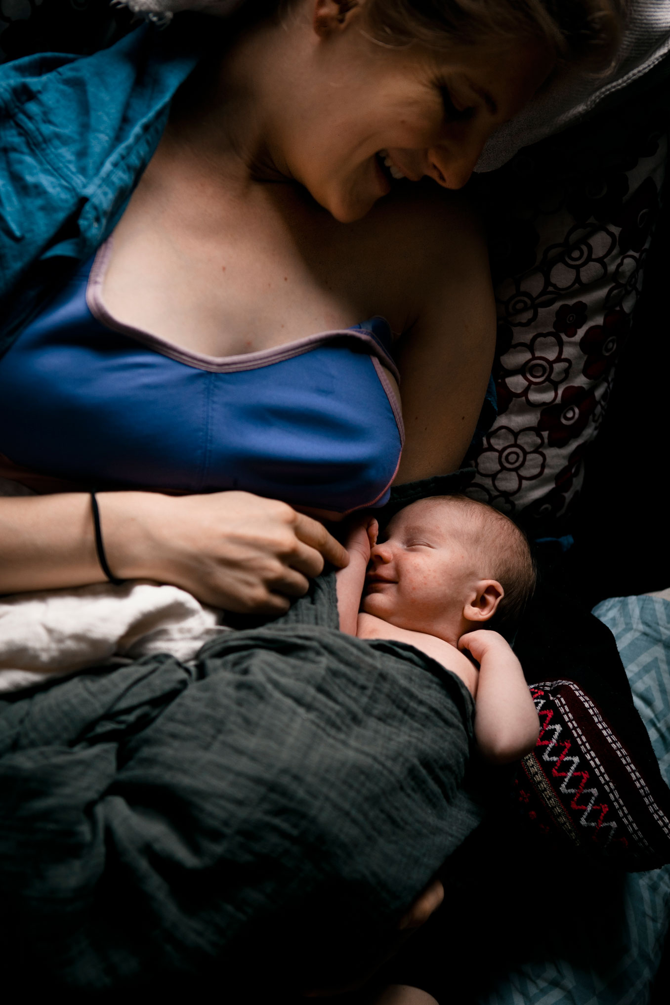 Neugeborenenfotos Berlin - Im Bett lächtelt junge Mama lächelt ihr Neugeborenes an