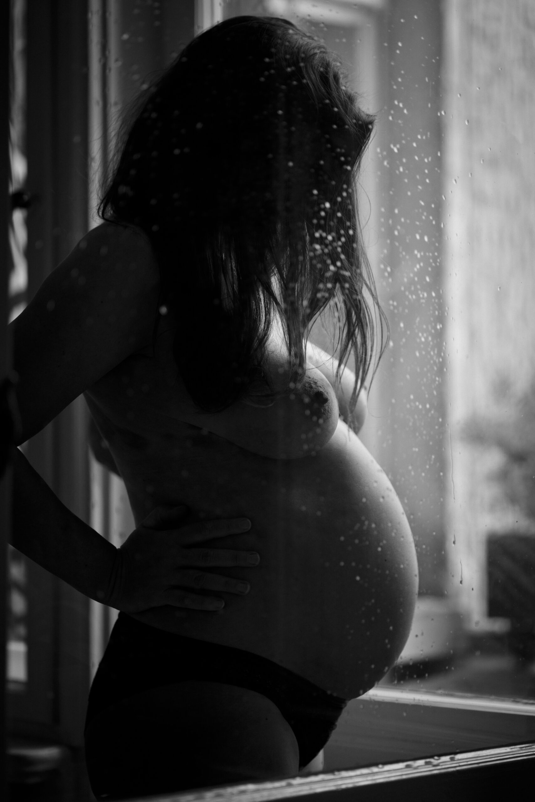 Schwangerschaftsfotos Berlin - Schwangere oben ohne hinter nasser Fensterscheibe