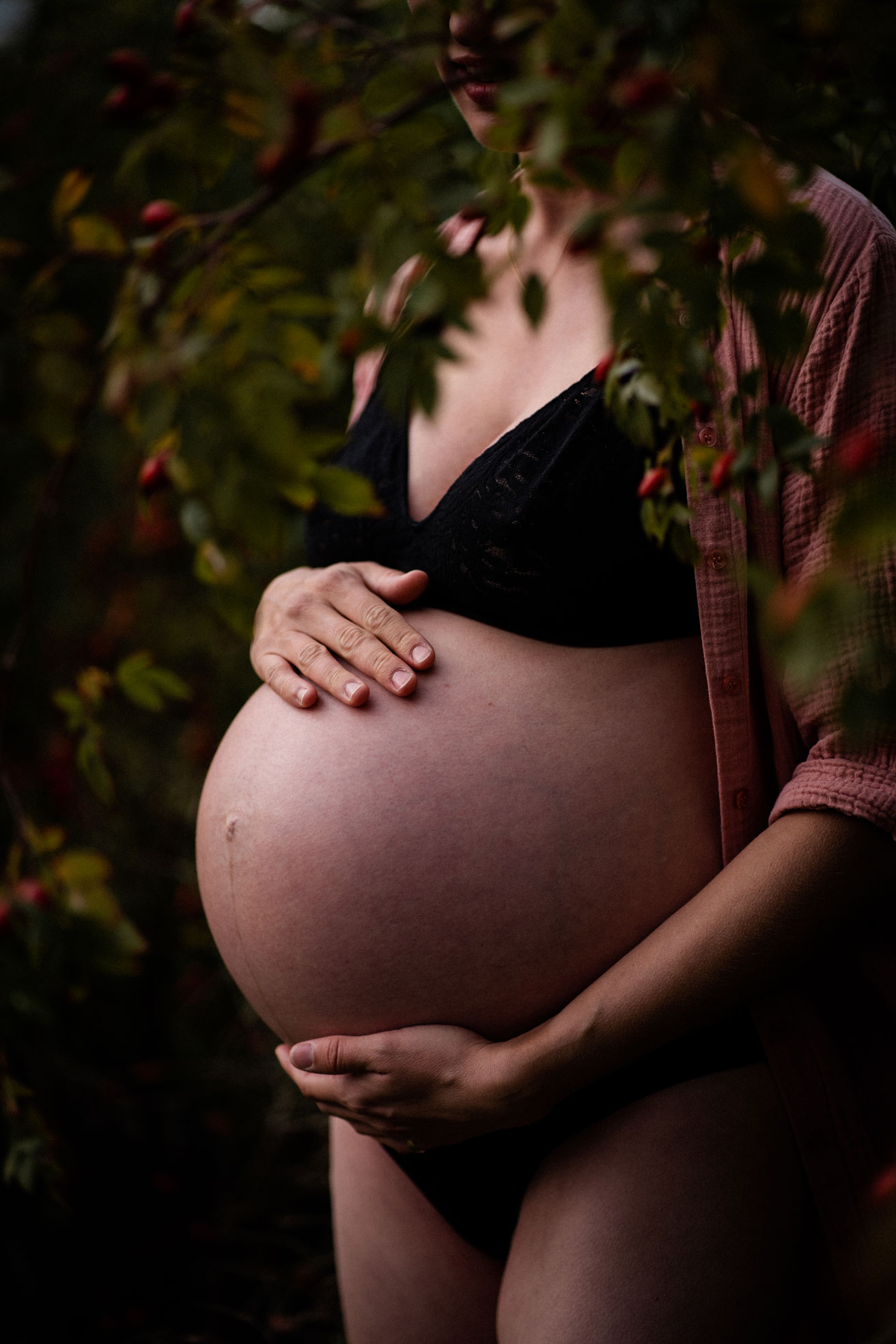 Schwangerschaftsfotos Berlin _ Schwangere mit nacktem Babybauch hinter Hagebuttenstrauch Tempelhofer Feld